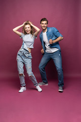 Active young couple of friends having good time, dancing, laughing together on pink background