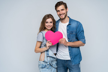 Couple smiling at camera holding a heart on white background.