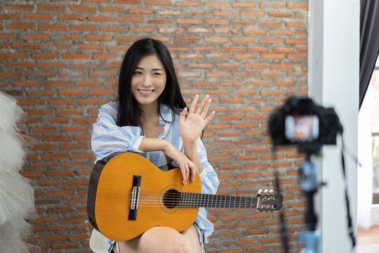 Attractive emotional smiling Asian Thai woman singing and playing acoustic guitar. Beautiful woman singer playing musical instrument indoors. People, music, joy and fun , she looks at camera