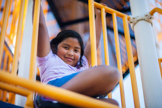 An active young girl hanging from the bars in a jungle gym or kids playground.