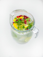 Lemonade pitcher with lemon slices, mint leaves, red berries and ice on glass jug. View with copy space