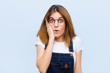 young pretty woman feeling shocked and astonished holding face to hand in disbelief with mouth wide...