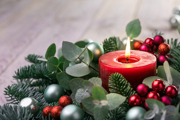 Christmas candle with fir branches and eucalyptus leaves on rustic wooden background  -  Advent time