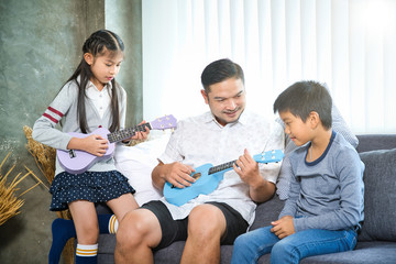 Happy elementary age Asian little kid is smiling  while playing a ukulele during a private music...