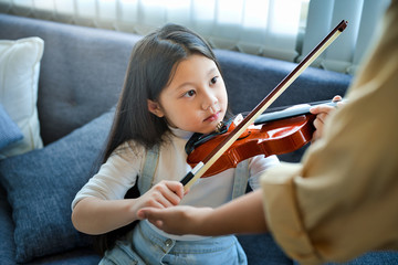 Asian kid learning and practising  to play violin at home