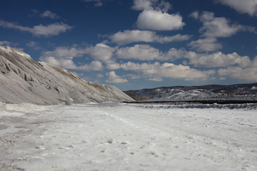 Hills of rubble on the background of a blue sky with clouds on a winter sunny day. Mining industry.