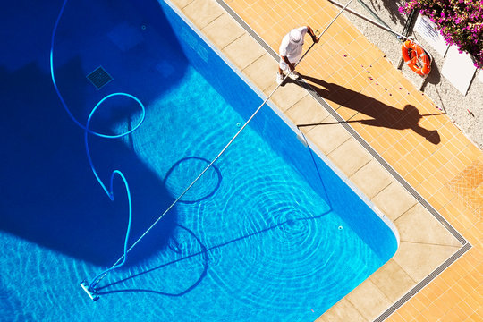 utility worker cleaning the swimming pool with vacuum equipment	