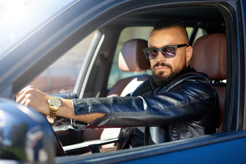 Confident stylish bearded man in sunglasses driving a car