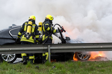 Feuerwehrmänner löschen ein brennendes Auto