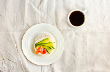 Rice crispy cakes with avocado and fresh salted salmon. Cup of coffee. Top view. Space for text. High protein and low carbohydrate meal. White linen tablecloth background