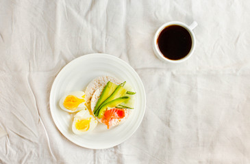 Rice crispy cakes with avocado and fresh salted salmon. Cup of coffee. Top view. Space for text. High protein and low carbohydrate meal. White linen tablecloth background