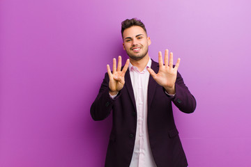 young hispanic man smiling and looking friendly, showing number nine or ninth with hand forward,...