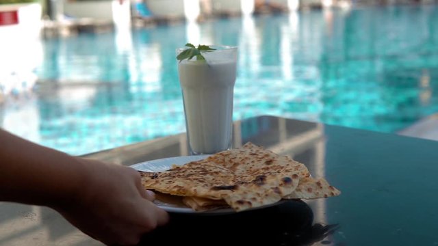 Female hand serving a Turkish pancake and ayran near pool, vacation pool