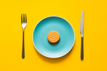 A round cookie with holes lying on colored blue plate with knife and fork on yellow background. Top...