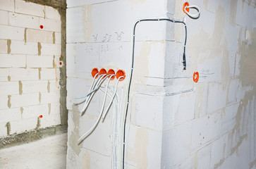 Orange, round junction box mounted in the white wall with protruding electric cables.
