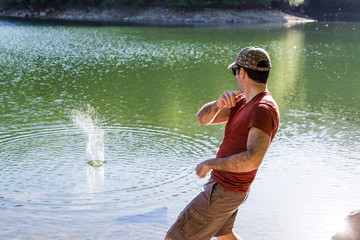 Hiker throwing stones in a lake at sunset