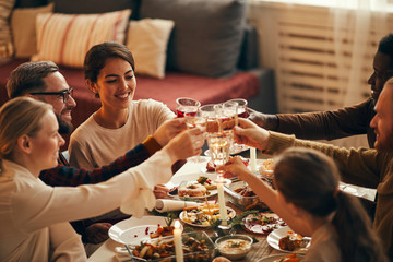 High angle view at elegant young people clinking champagne glasses while enjoying Christmas dinner at home, copy space