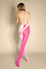 Back view of a blonde lady in pink two-tone tights. The slim shirtless woman with a short hairdo is posing on tiptoes on the beige background. 