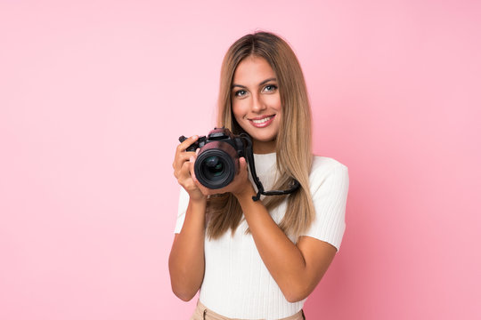 Young blonde woman over isolated pink background with a professional camera