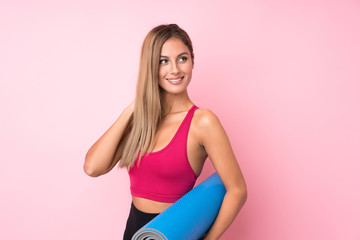 Young sport blonde woman over isolated pink background with a mat