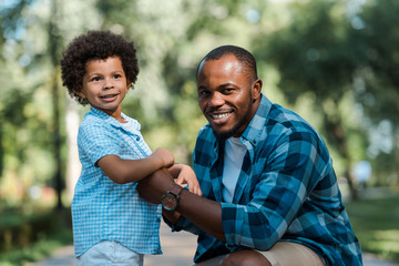 cute curly african american kid holding hands with cheerful father