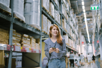 Young asian woman customer walking around a furniture warehouse store with a smartphone.