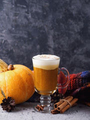 a glass of pumpkin spiced latte on the table with a colorful scarf and cinnamon and autumn leaves