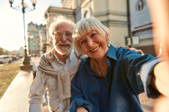 Happy moments together. Cheerful senior couple in casual clothes making a selfie while sitting on the bench outdoors