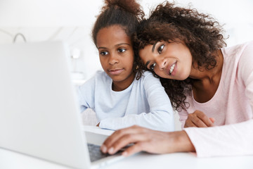 Image of african american woman and her daughter using laptop at home
