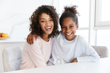 Image of african american woman and her little daughter hugging at home