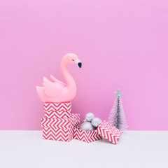 Plastic pink flamingo bird, silver decoration balls, three sized gift boxes and fir tree on white and pink background
