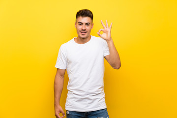 Young handsome man over isolated yellow background surprised and showing ok sign