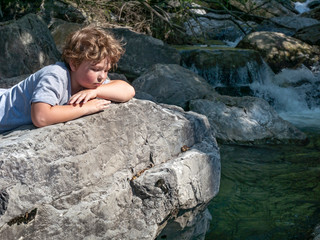 boy seated next to mountain waterfall
