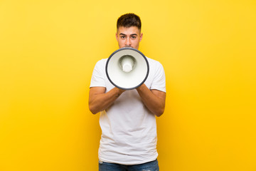 Young handsome man over isolated yellow background shouting through a megaphone
