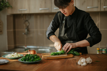 Portrait of female chef preparing a recipe in the kitchen with vegetables. Woman cook chopping spinach leaves for vegetarian dish.