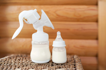 Breast pump and bottle with breast milk for baby on wooden background. Maternity and baby care...