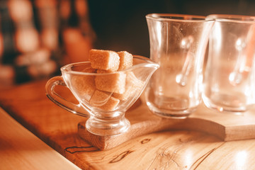 a Cup of clear glass tea, a small sugar bowl with a square of yellow sugar, and a teapot of tea on the wooden table.