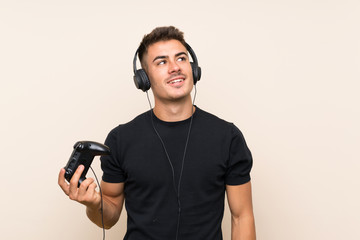 Young handsome man playing with a video game controller over isolated background looking up while smiling © luismolinero