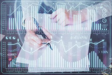Hand taking notes in notepad. Forex chart holograms in front. Concept of research. Multi exposure