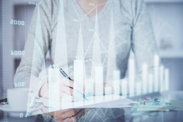 Hand taking notes in notepad. Forex chart holograms in front. Concept of research. Multi exposure