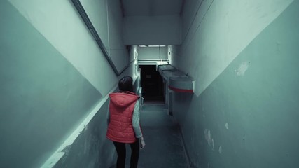 Back view of young brunette in red sleeveless jacket descends down long staircase in dark old corridor, tracking shot. - Powered by Adobe