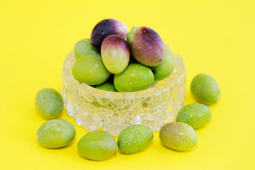 natural fresh round green and brown olives in a decorative glass plate on a yellow background
