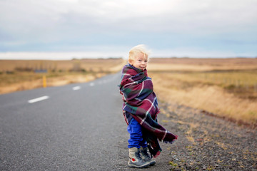 Beautiful child, standing on a road on a very windy day, wrapped in scarf, watching the sunrise in Iceland