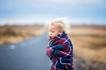 Beautiful child, standing on a road on a very windy day, wrapped in scarf, watching the sunrise in Iceland