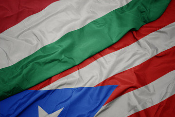 waving colorful flag of puerto rico and national flag of hungary.