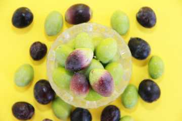 natural fresh round green and brown olives in a decorative glass plate on a yellow background