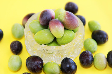 natural fresh round green and brown olives in a decorative glass plate on a yellow background