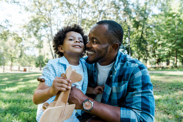 happy african american father looking at cute son holding wooden toy biplane