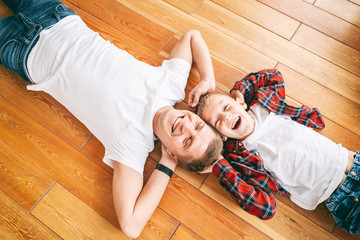 Father and son, 8 years old boy in checkered shirts lie head to head on a wooden floor, top view