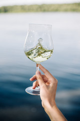 Female hand holds a glass with wine on the background of the river